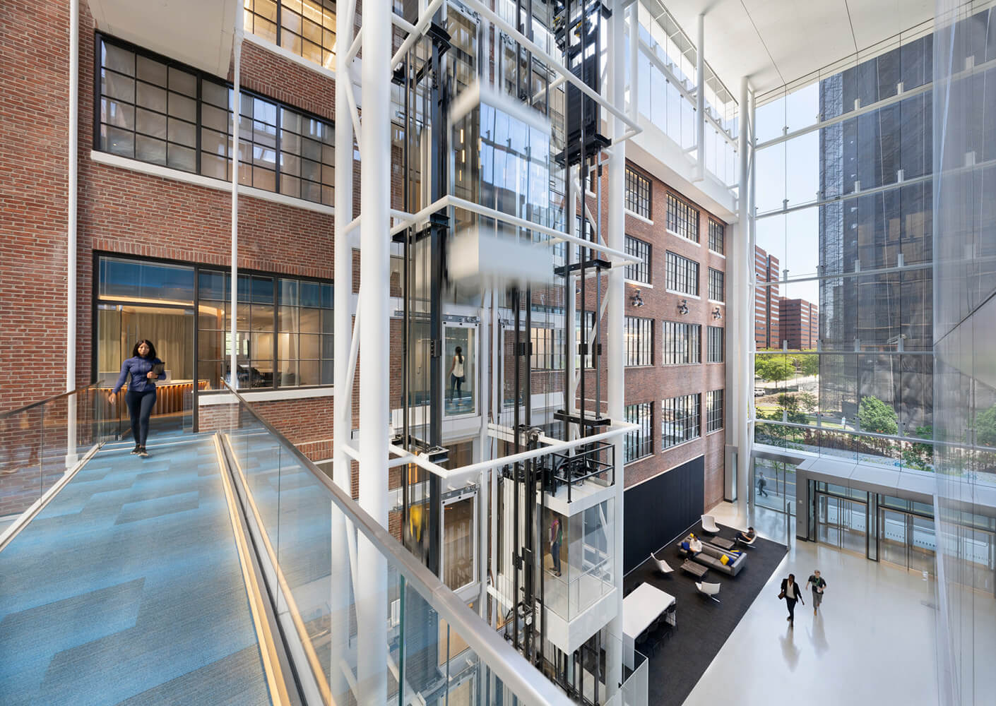 interior atrium with a glass walkway and retrofit elevator adjacent to a historical brick building