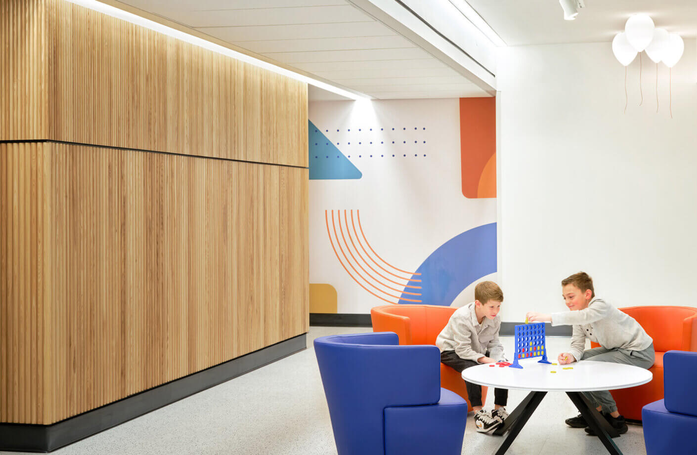 Children playing a board game in a modern, vibrant lounge area with three balloon-shaped lights overhead