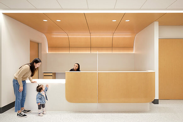 Modern, warm clinic reception with staff, mother, and toddler interacting.