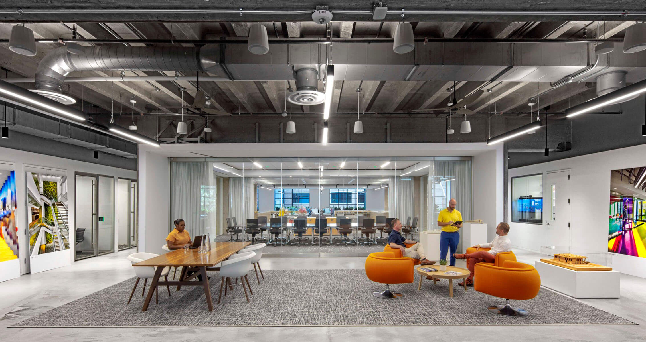 Creative office with people sitting in lounge chairs and a transparent conference room in back