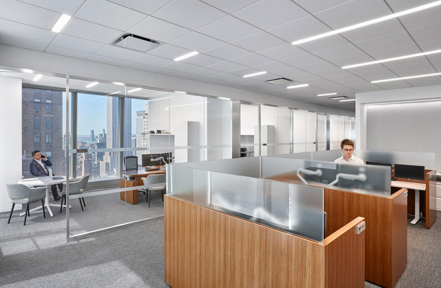 person working at open office desk and person on phone in conference room in back