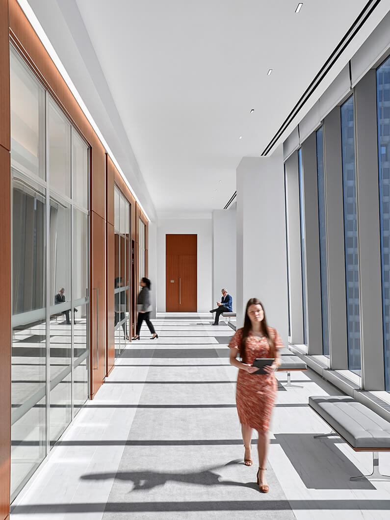 Person walking down an office hallway with large windows to the right