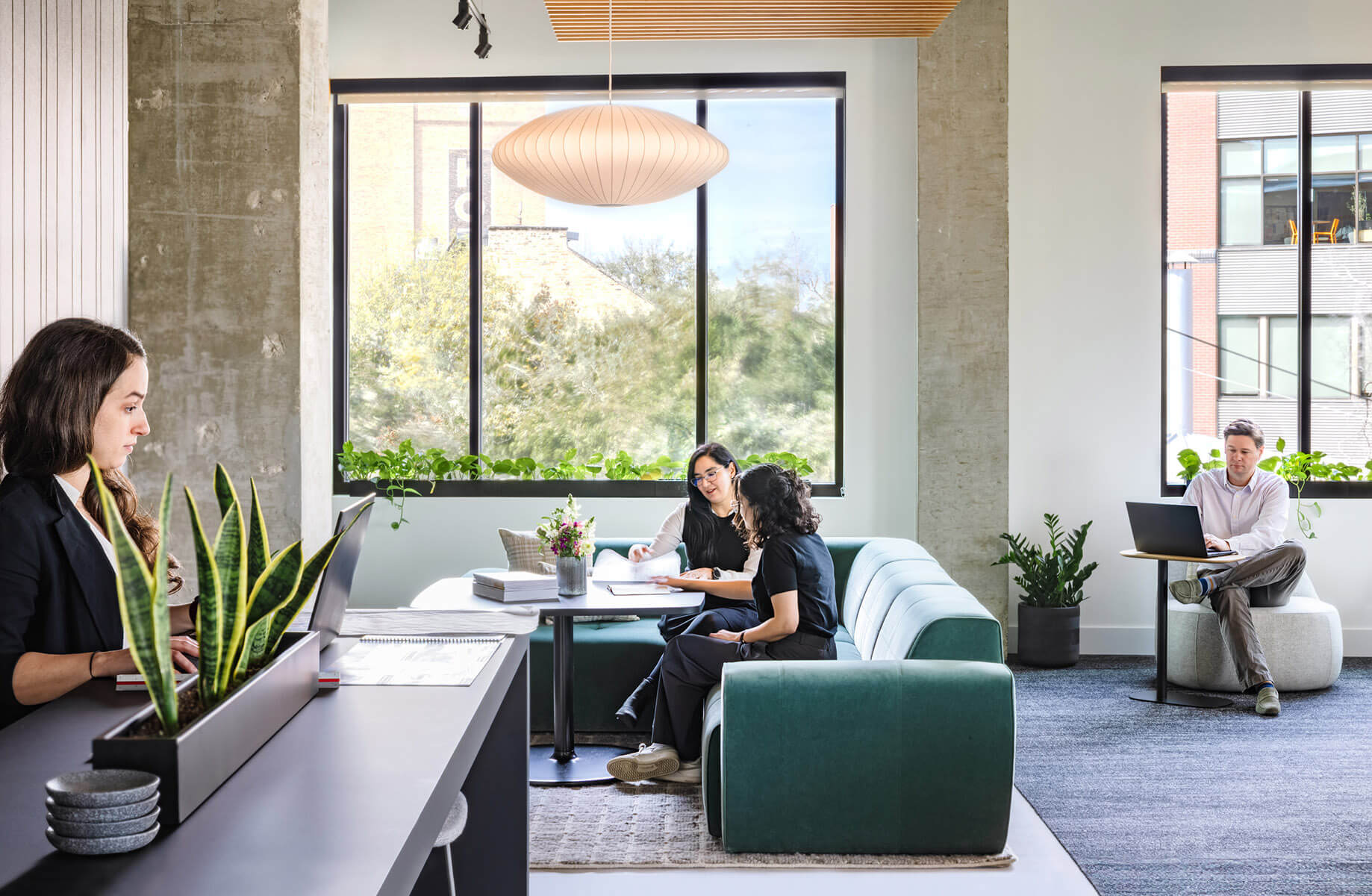 Designers work on a communal couch by a large window, bathed in abundant natural light