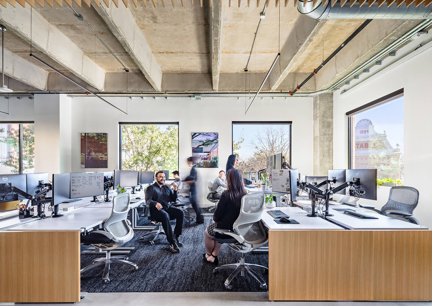 The design team works at their desks, arranged in an open concept under an exposed ceiling. The natural materiality like wood on the desks and concrete on the ceiling is warmed by abundant light.