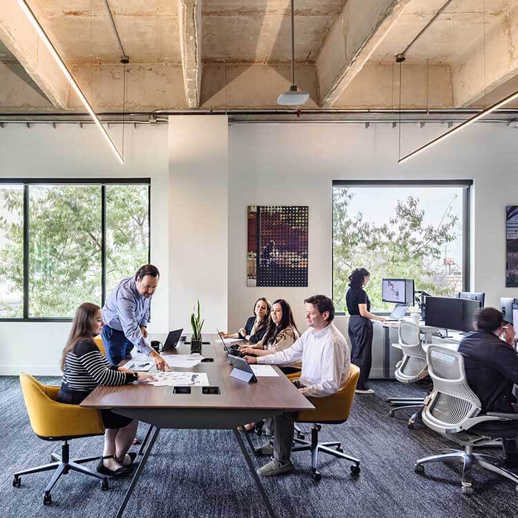 Designers work on a communal couch by a large window, bathed in abundant natural light