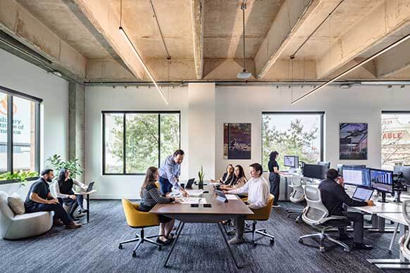 Designers work on a communal couch by a large window, bathed in abundant natural light