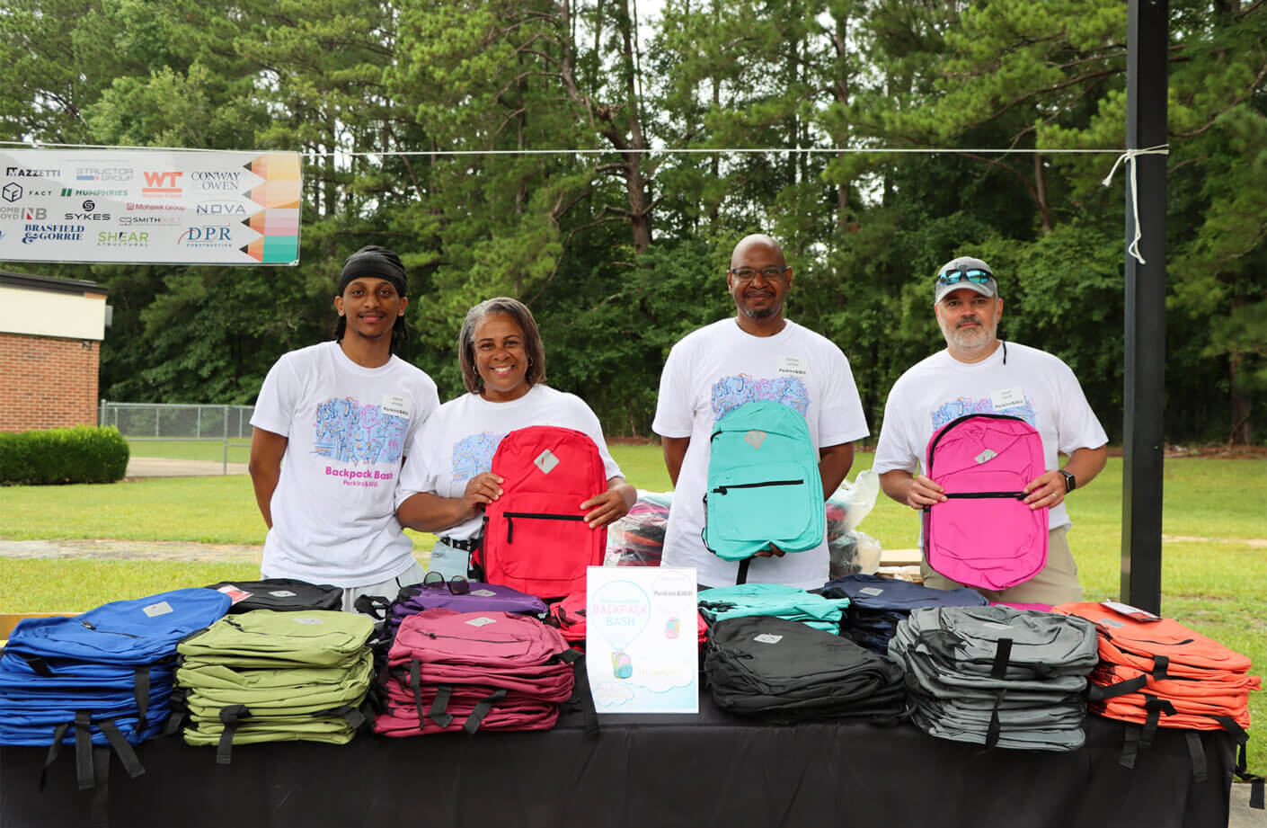 a group of people behind a table holding backpacks