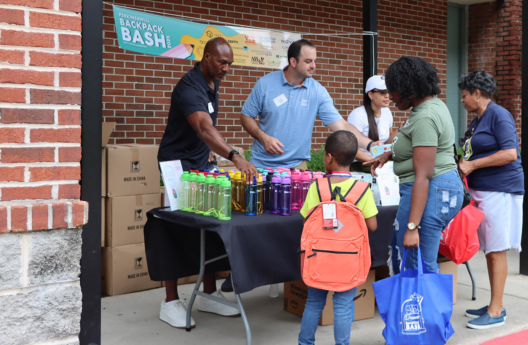 man behind a table handing out school supplies to kid