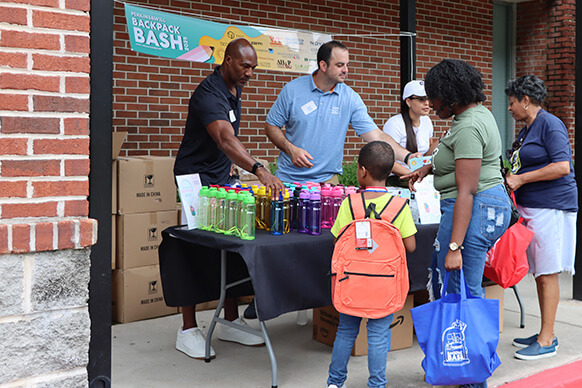 people behind a table handing school supplies to a student