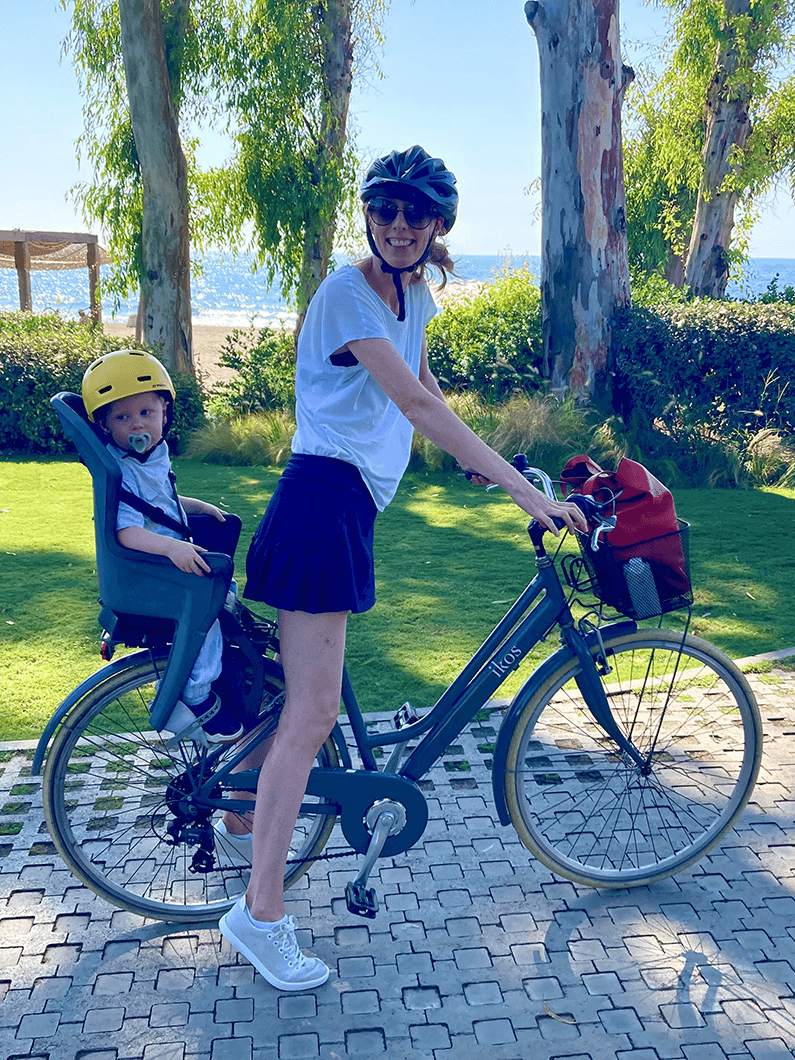 Woman on bicycle with child in bike seat outdoors on a sunny day by the water
