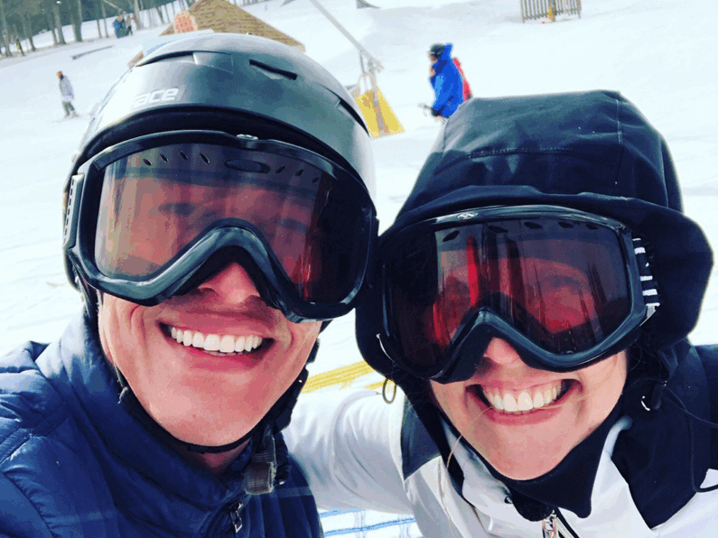 Two people smiling at the camera wearing ski goggles and helmets on the slopes.