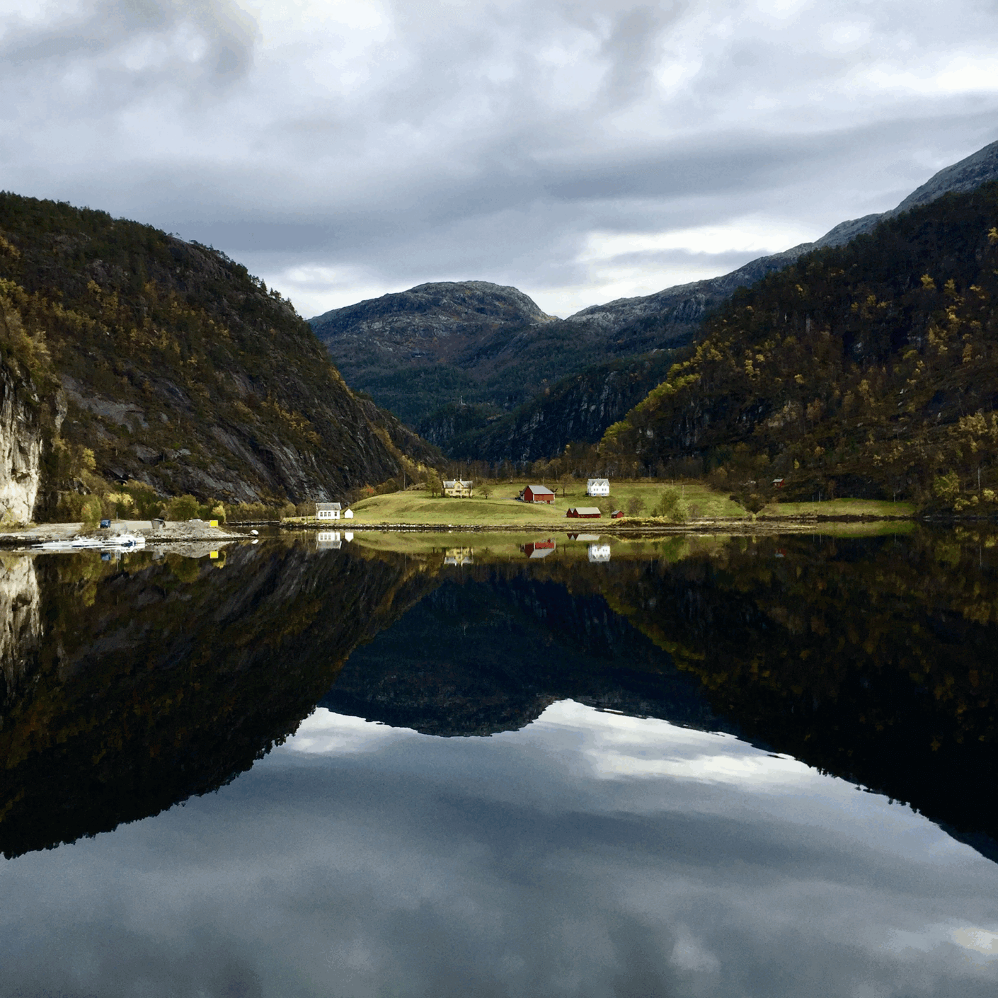 Image of small village with cloudy sky reflected in water surrounded by mountains.