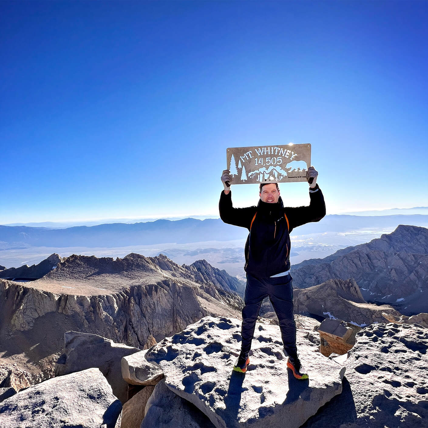 Man on top of mountain holding sign