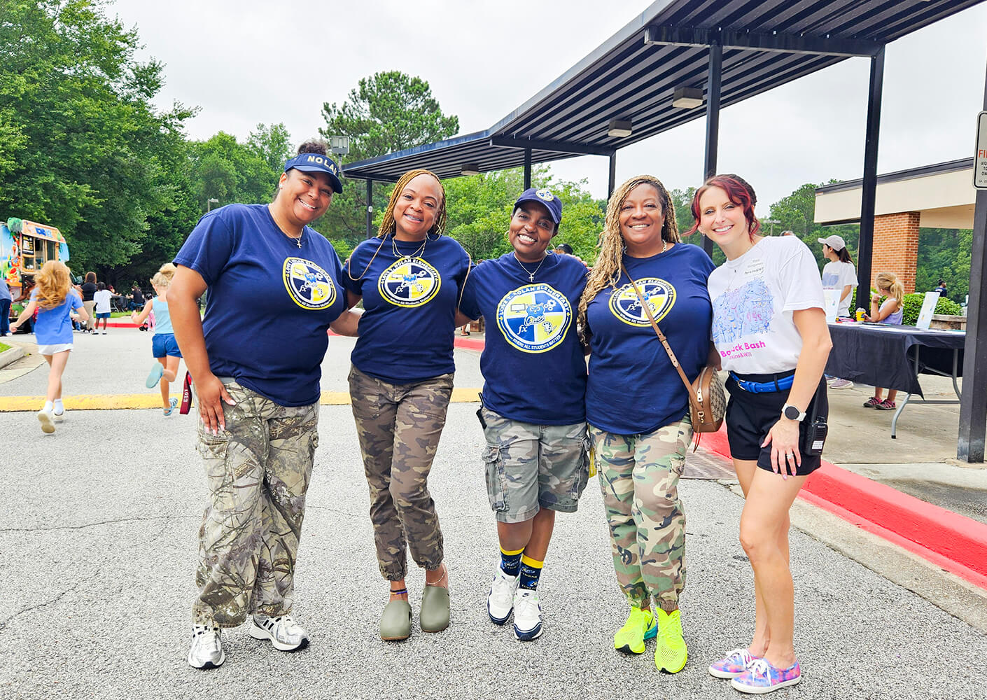 Five women smiling in front of an elementary school