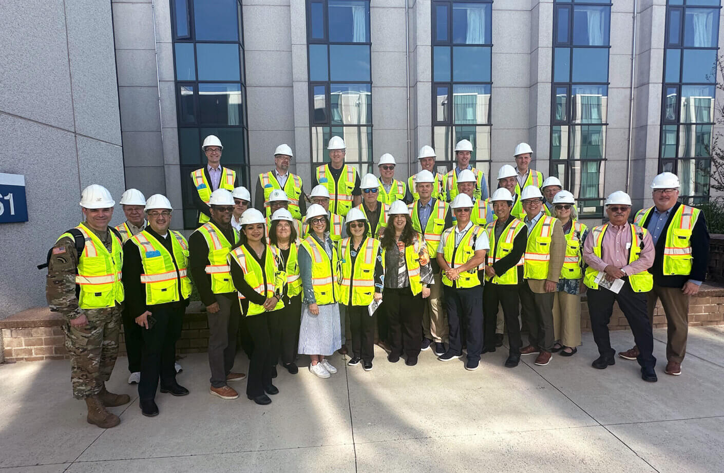 Group of people in safety vests and helmets outside a building, ready for a construction site visit.