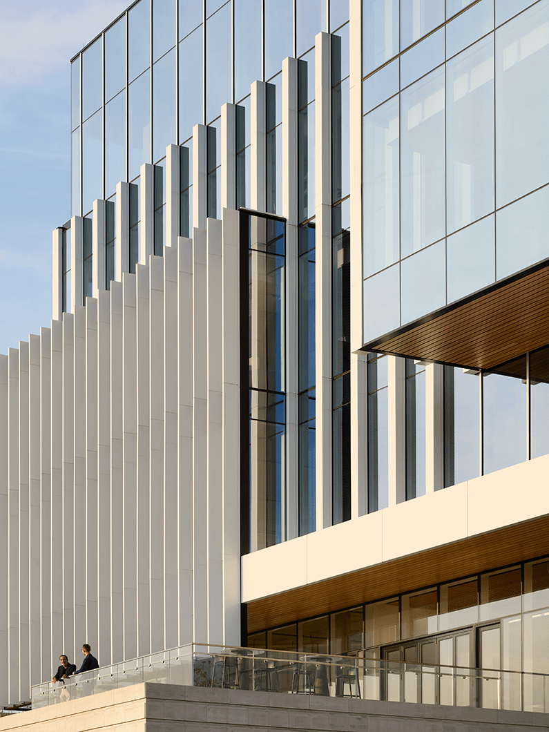 Modern glass building exterior with two people on a balcony, highlighting architectural design and clean lines.