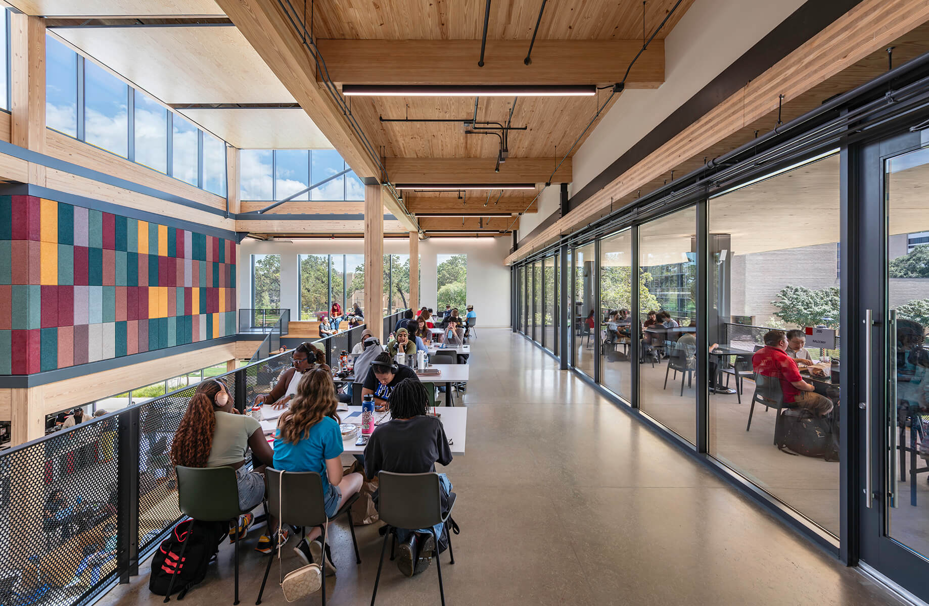 Modern university cafeteria with students studying, featuring large windows and colorful wall design.