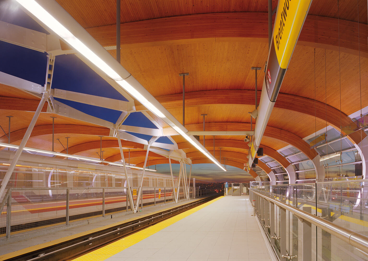Modern train station with wooden ceiling and empty platform at dusk.