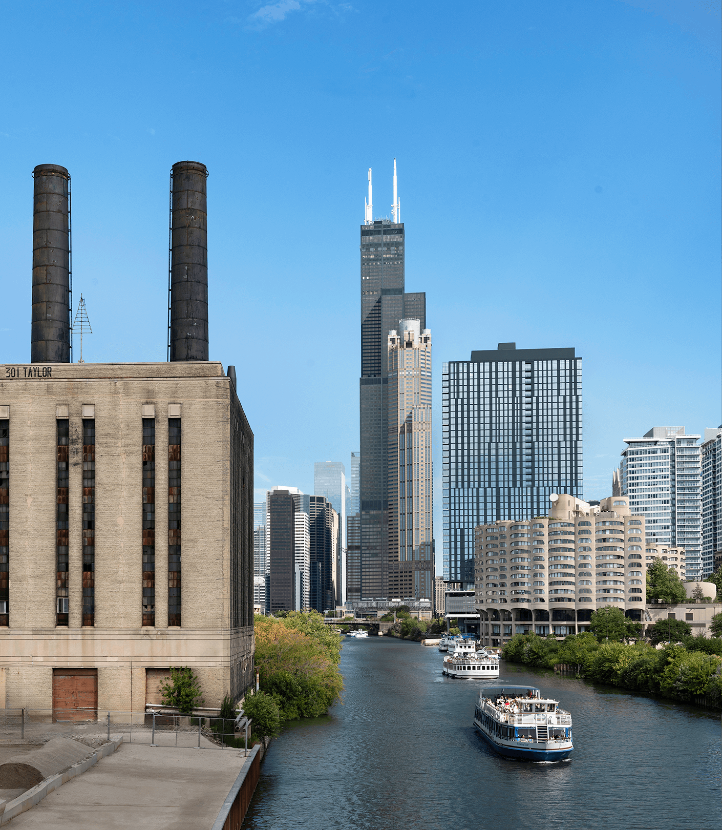 Chicago cityscape with skyscrapers, riverboats on the water, and a clear blue sky.