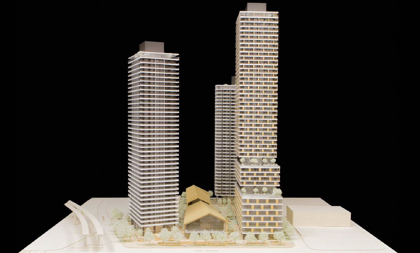 Architectural model of modern high-rise buildings with a central atrium structure, viewed against a black background.