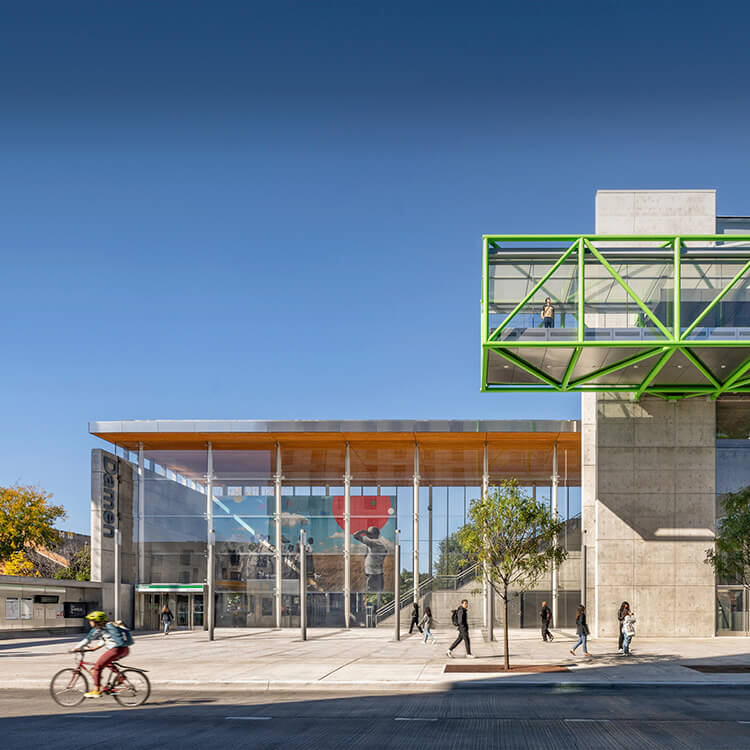 Modern transit station with green walkway, cyclists, and pedestrians under a clear blue sky.