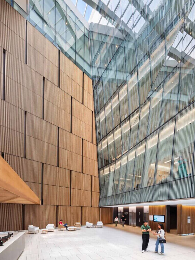 Modern atrium with wood and glass design, featuring seating area, high ceilings, and natural light.