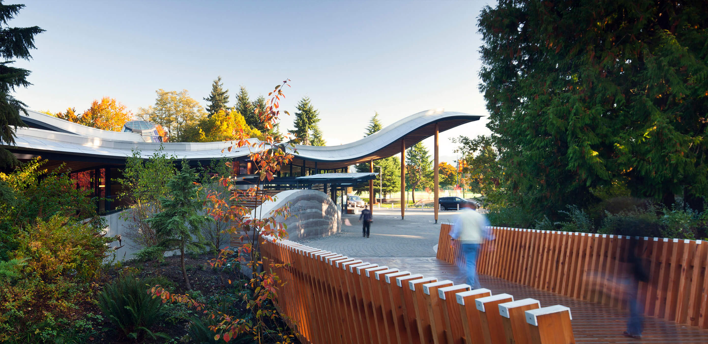 Curved building with wooden bridge in lush forest setting.