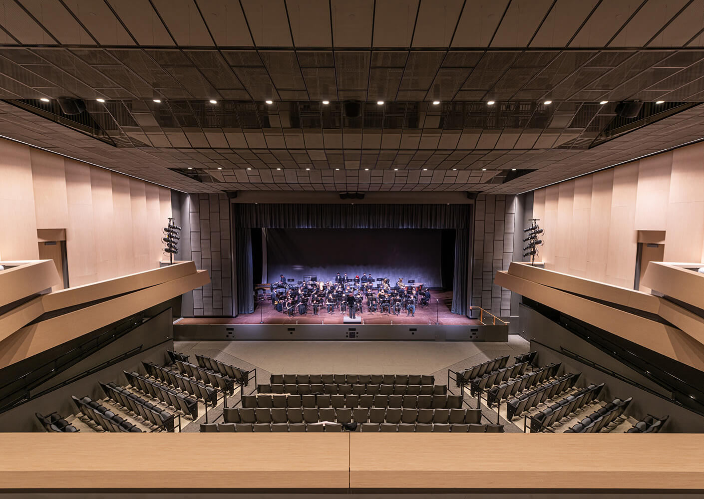 Wide view of a concert hall with an orchestra on stage, showcasing modern architecture and ample seating.