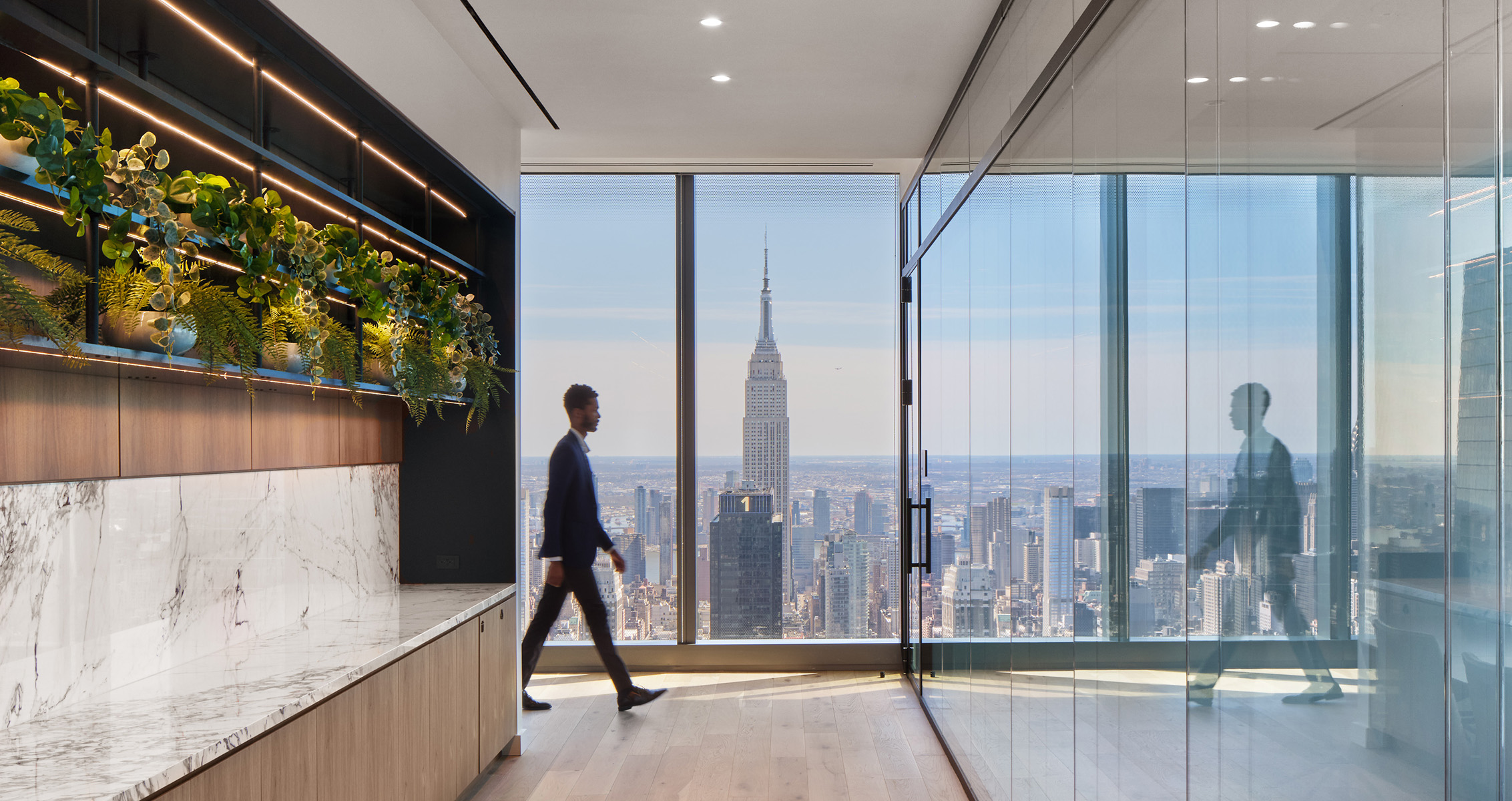 Man walking in modern office with plants and Empire State Building view in background.