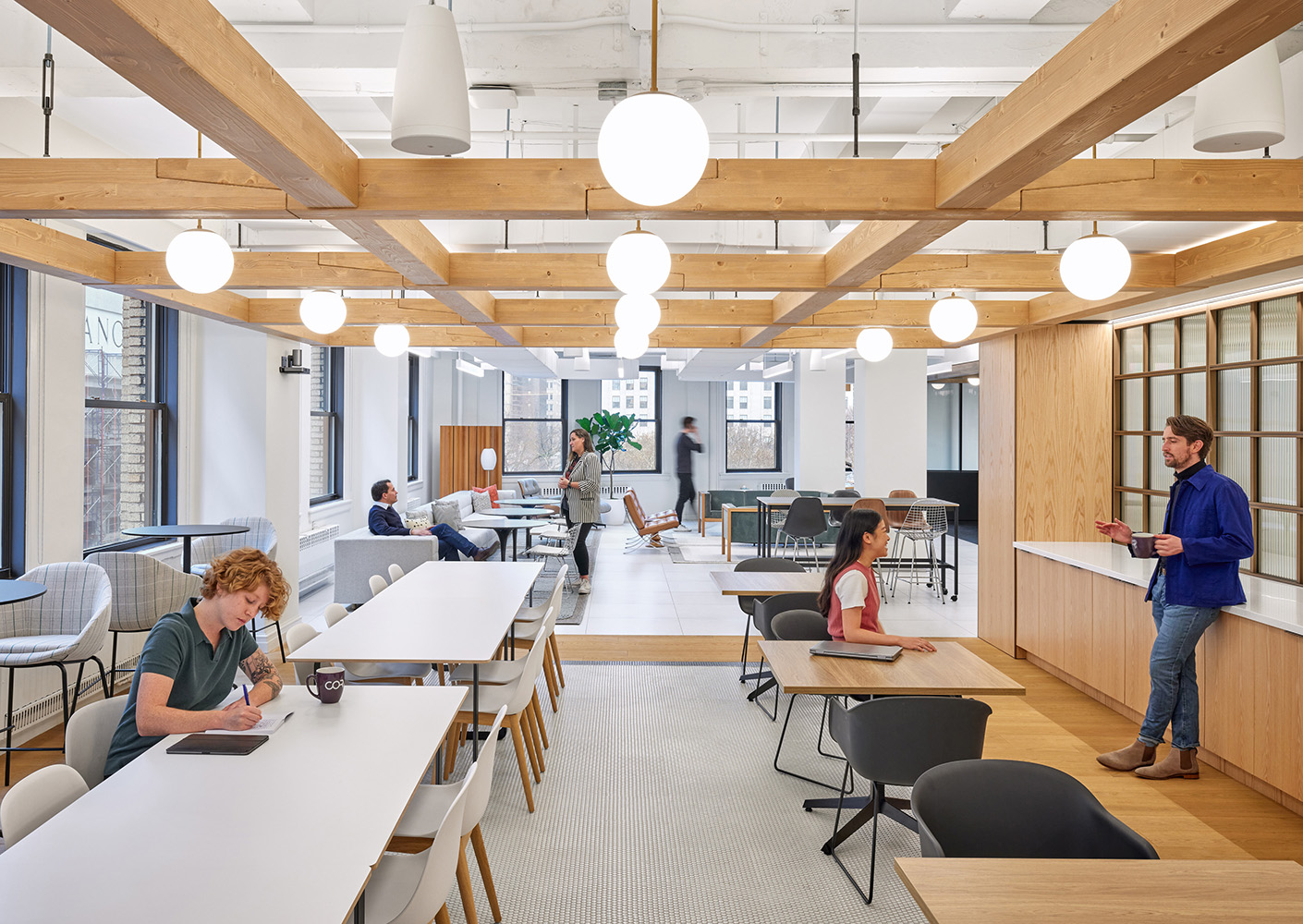 Modern office space with people working, collaborating, and conversing in a bright, open environment.
