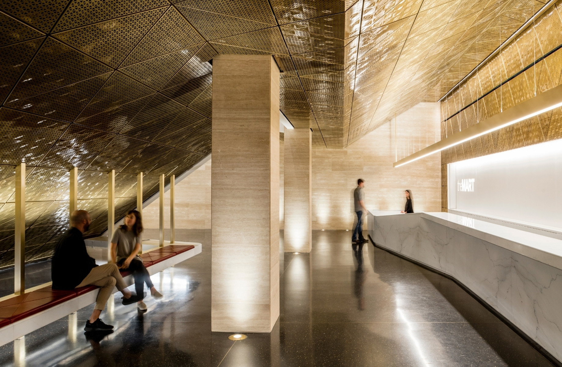 Modern office lobby with sleek marble reception desk, geometric ceiling design, and people chatting on benches.