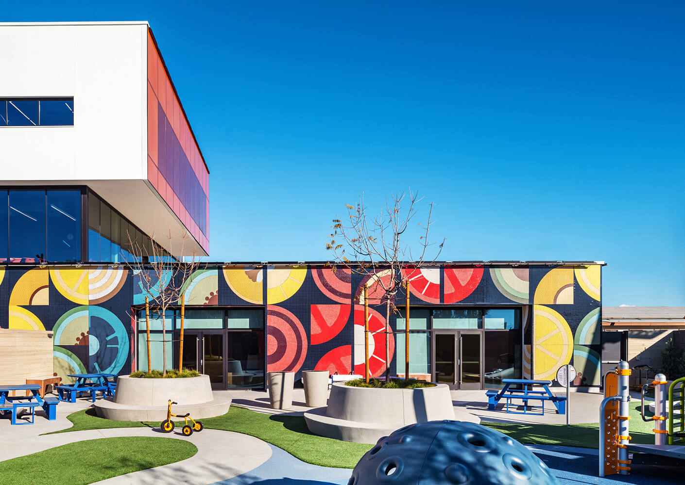 Colorful clinic playground with mural, vibrant patterns, and modern architecture under a clear blue sky.