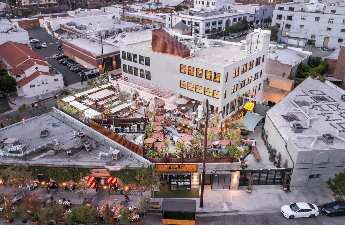 Aerial view of a bustling rooftop restaurant with outdoor seating and cityscape background at dusk.