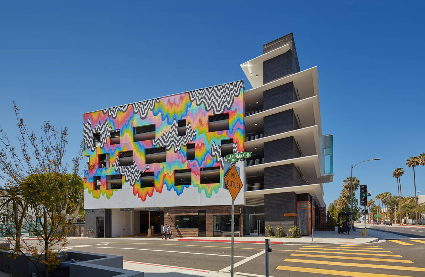 Colorful mural on modern building exterior, urban street view with blue sky.