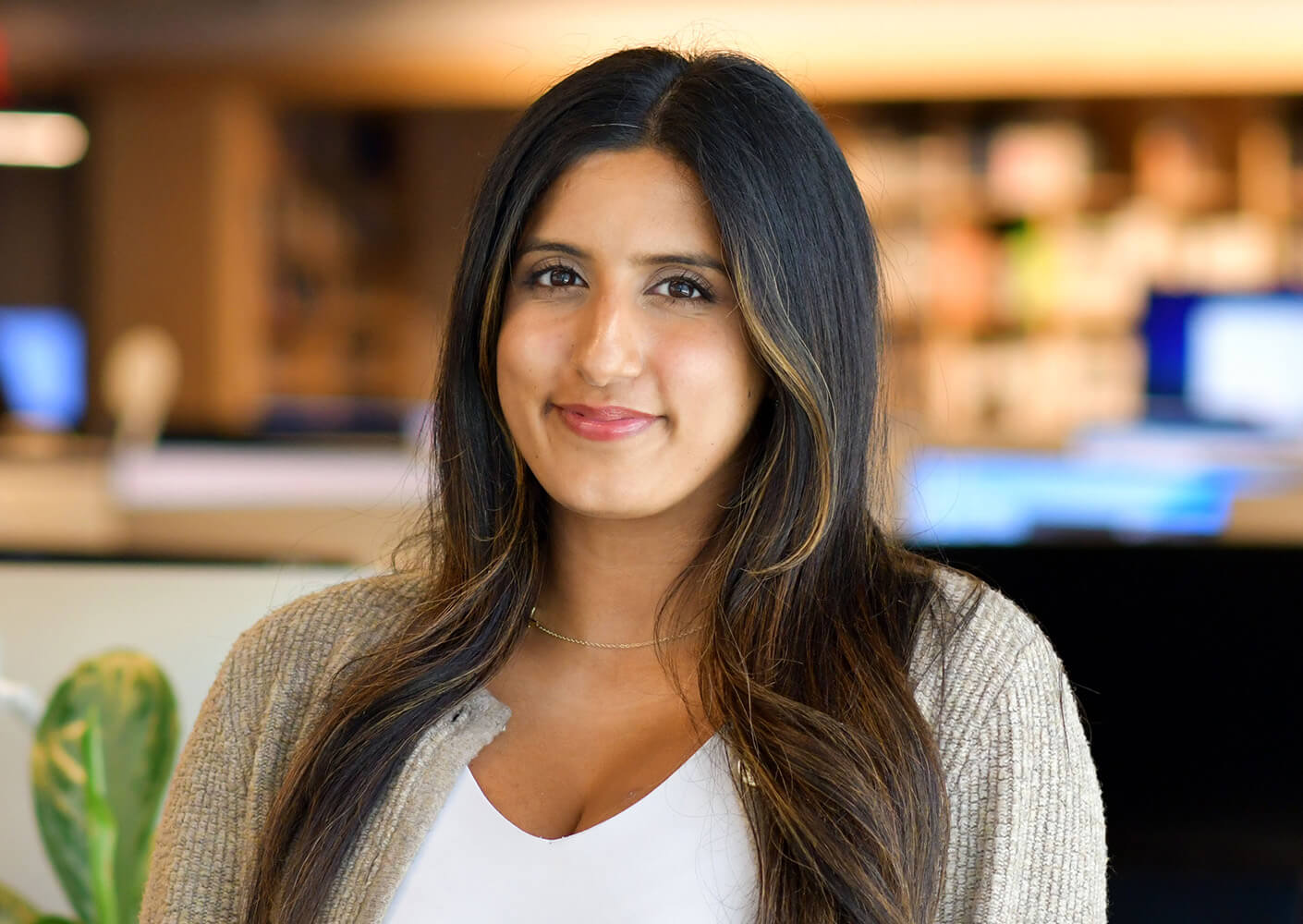 Woman smiling at the camera in a cozy indoor setting, wearing a white top and beige cardigan.