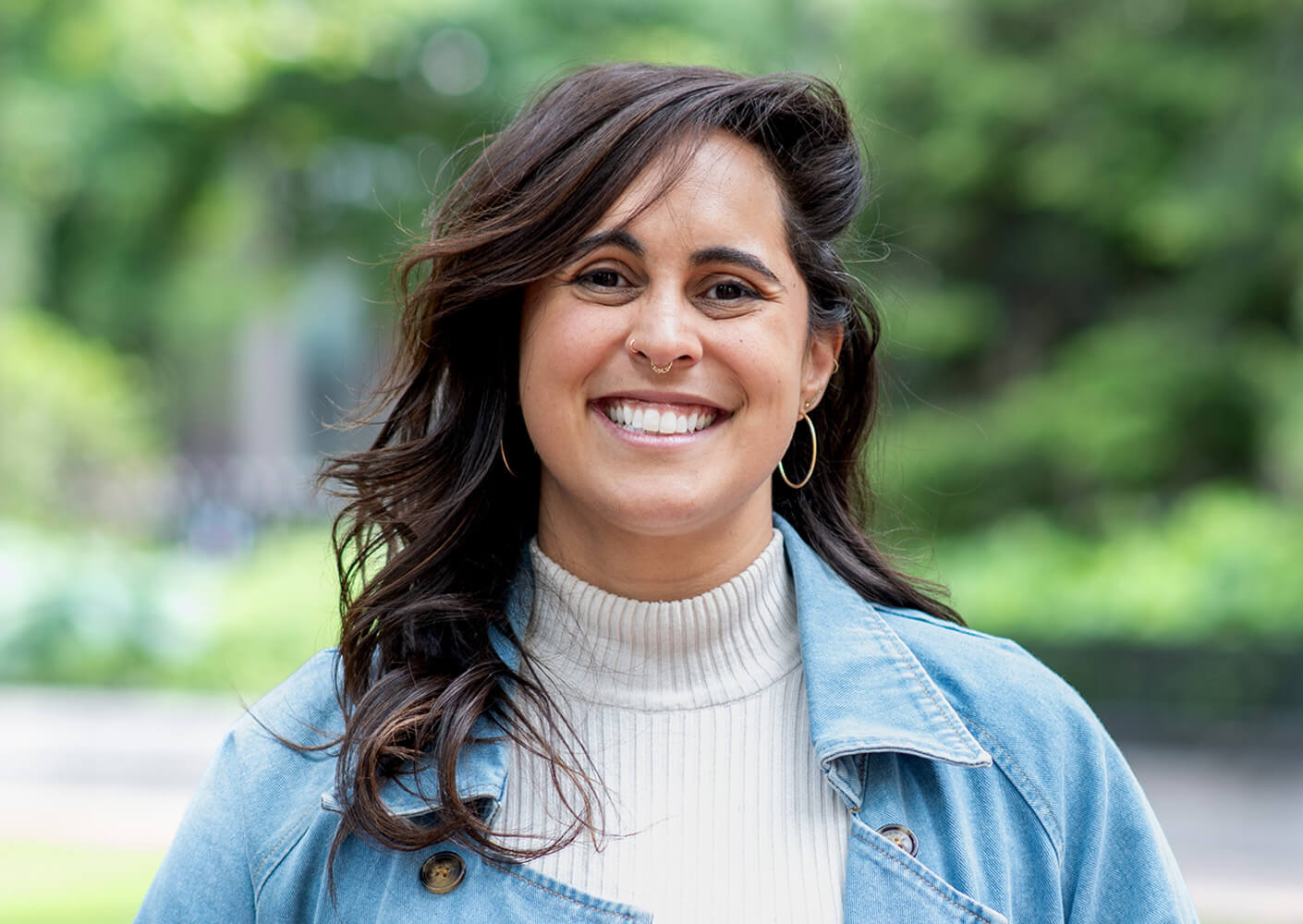 Smiling woman in a blue jacket outdoors, with blurred green background.