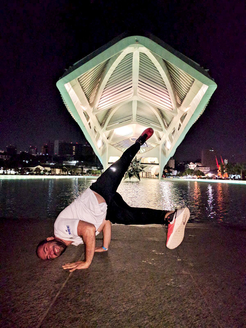 Man doing a breakdance freeze in front of an illuminated modern building at night.
