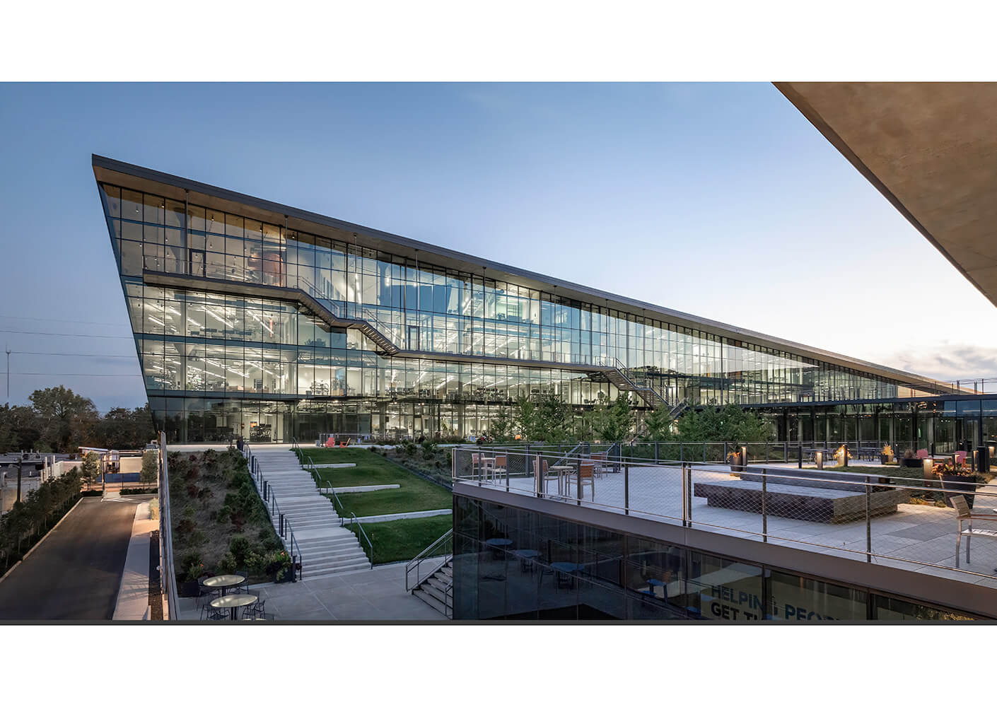 Modern glass building with outdoor seating and green landscaping.