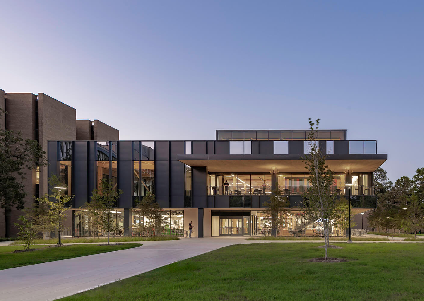 Modern two-story building at dusk with large windows and landscaped surroundings.