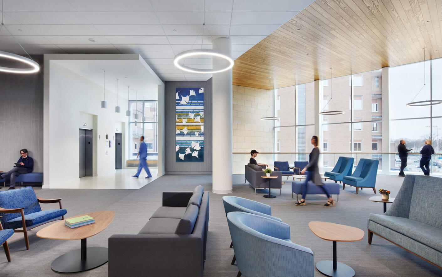 Modern hospital lobby with visitors and staff, featuring stylish seating and large windows.