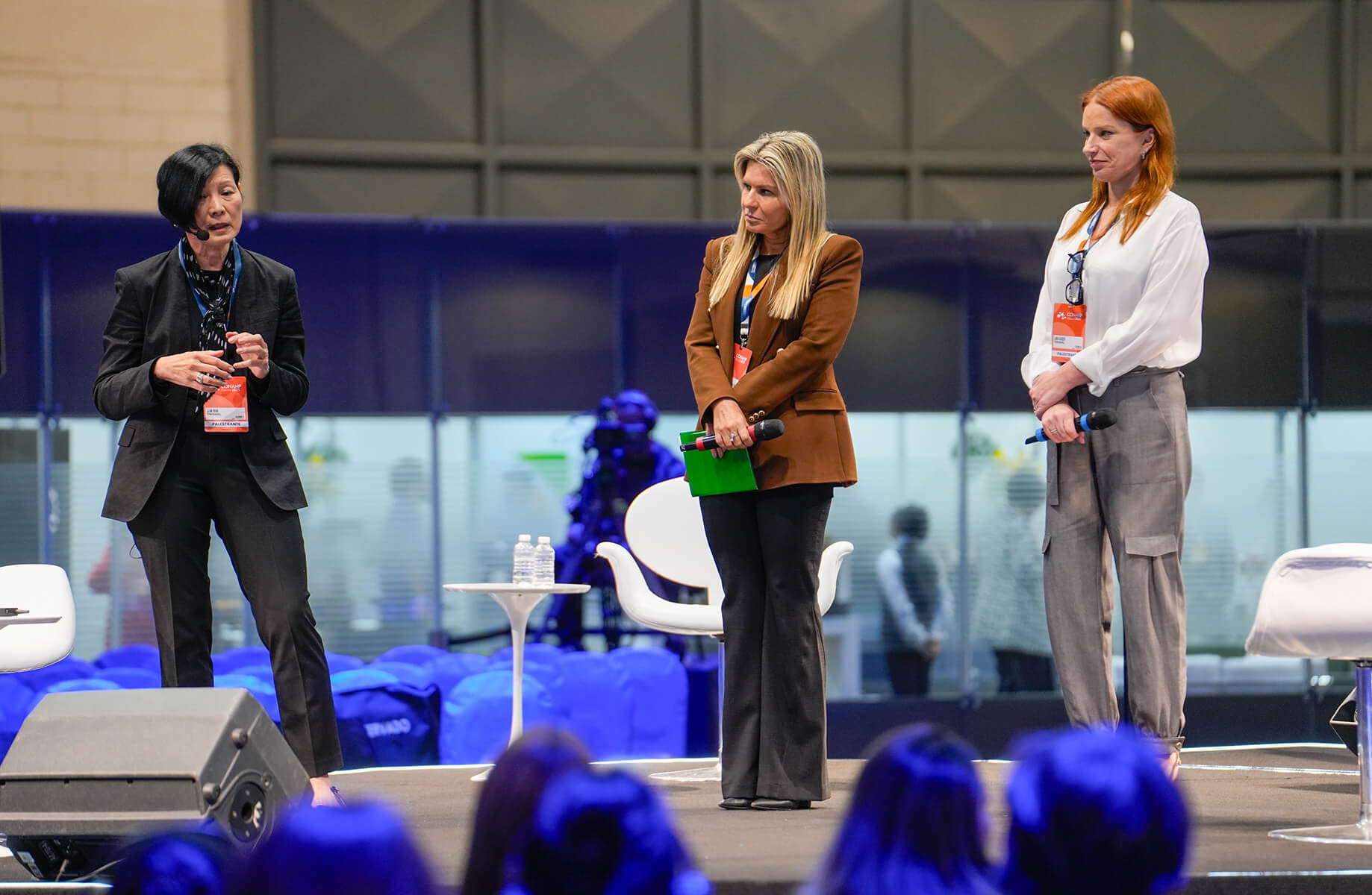 Three women presenting at a conference stage with microphones.