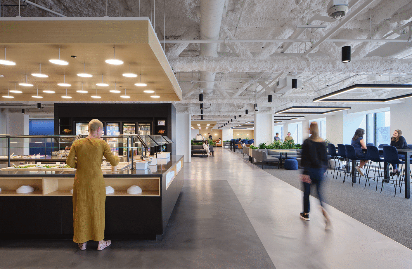 Modern office cafeteria with open seating and people dining.