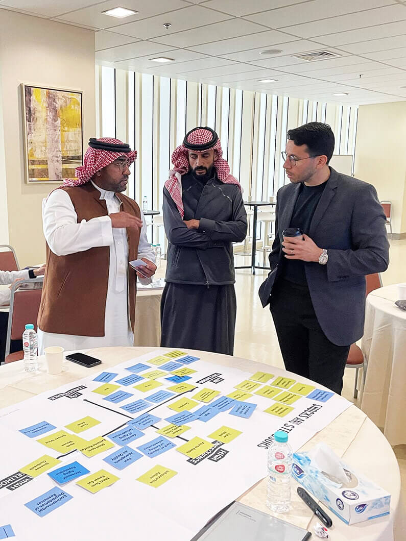 Three men discussing a project plan with notes on a table in a bright office setting.