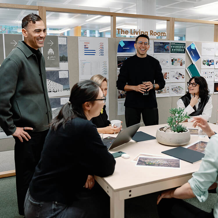Colleagues collaborate in a creative office meeting around a table with a laptop.