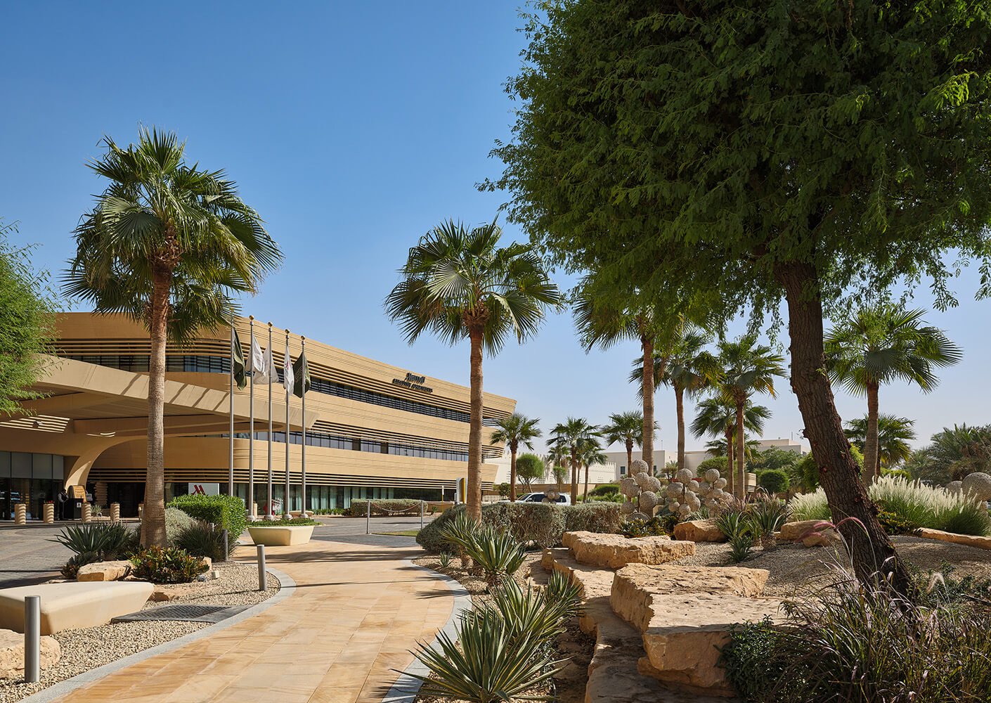 Modern building with palm trees and landscaped garden under a clear blue sky.