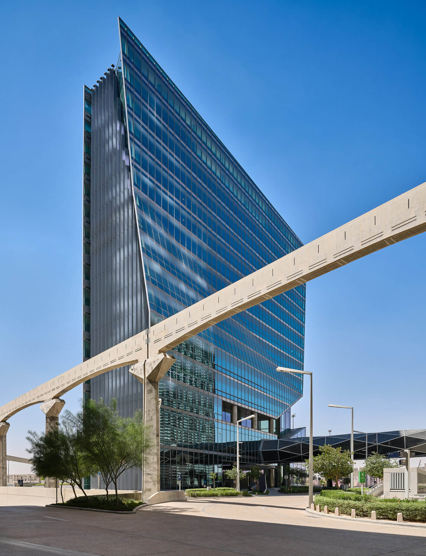 Futuristic glass building with blue sky and overhead monorail track.