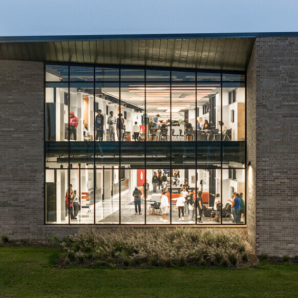 Two-story building facade with people visible through glass windows at dusk.