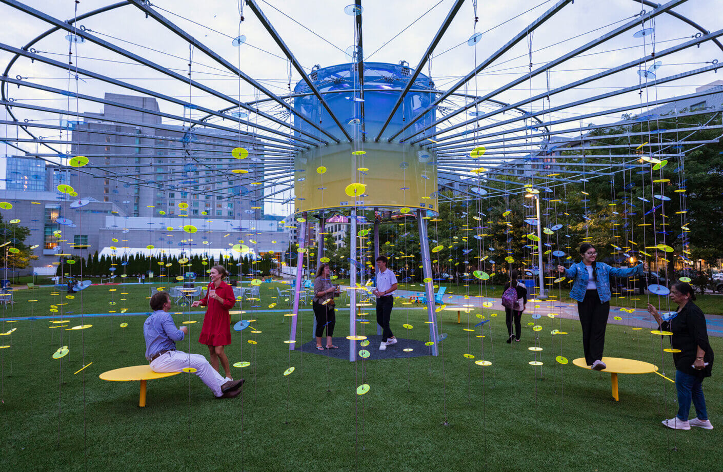 Interactive outdoor art installation with people enjoying colorful hanging discs.