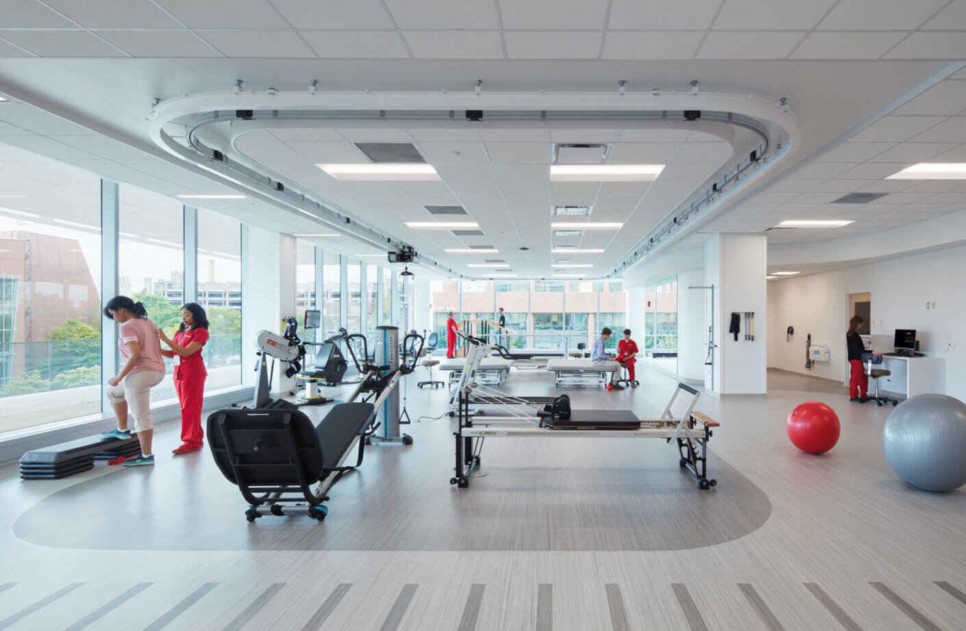 Modern rehabilitation gym with exercise equipment and people in therapy sessions.