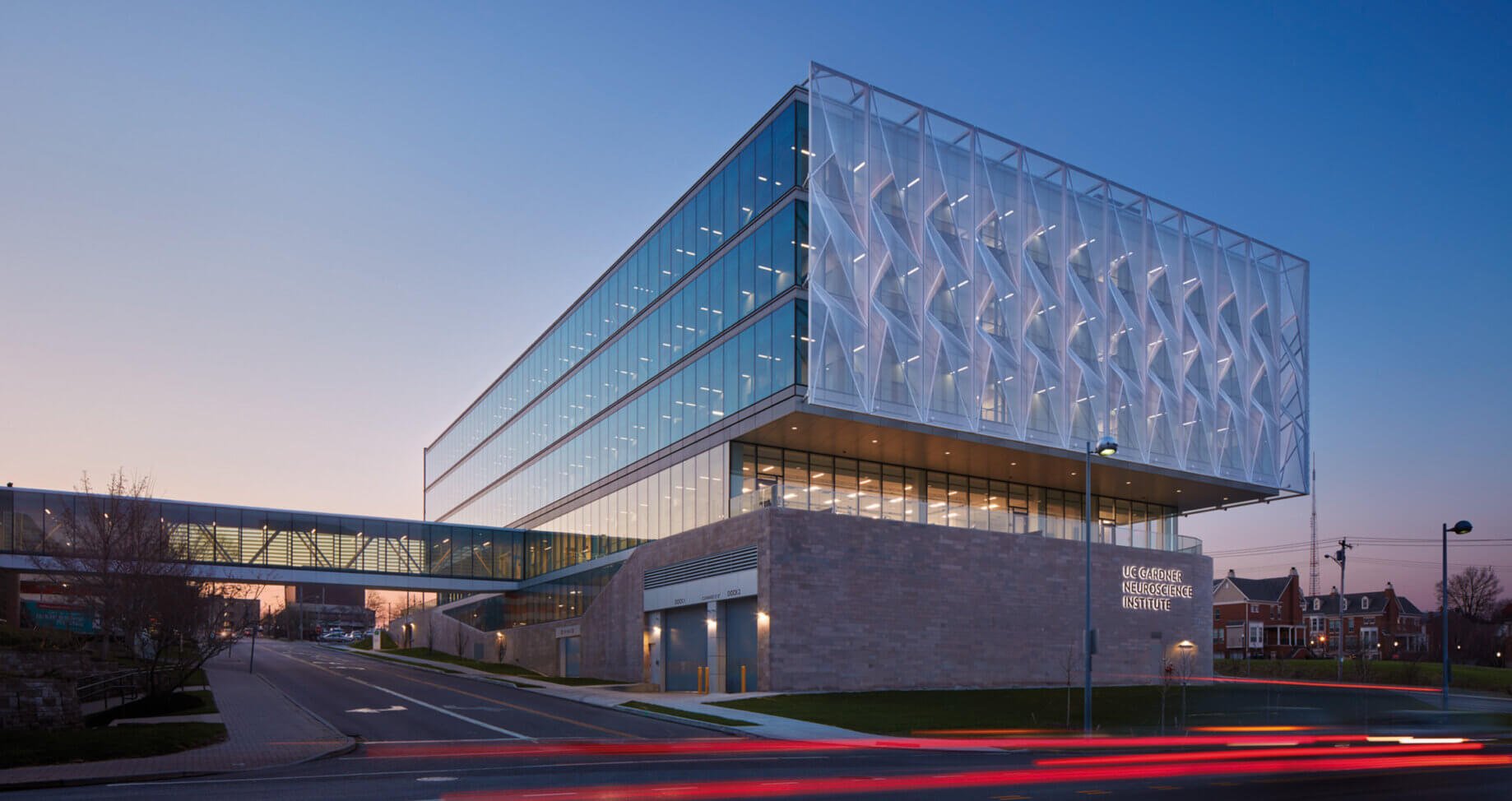 Modern glass building at dusk with bridge connecting over street.